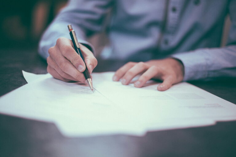 Hand met pen die een contract ondertekent aan tafel